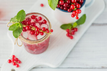 Glass jar of red currant soda drink on a white wooden table. Summer healthy detox lemonade, cocktail or another drink background. Low alcohol, nonalcoholic drinks, vegetarian or healthy diet concept.