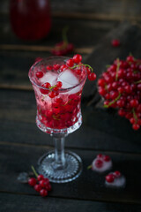 Glass of red currant cocktail or mocktail, refreshing summer drink with crushed ice and sparkling water on a dark wooden background