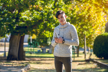 Young man in gray sweater in the park with smartphone and headphonesYoung man in gray sweater in the park with mobile phone and headphones