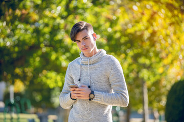 Young man in gray sweater in the park with mobile phone and headphones