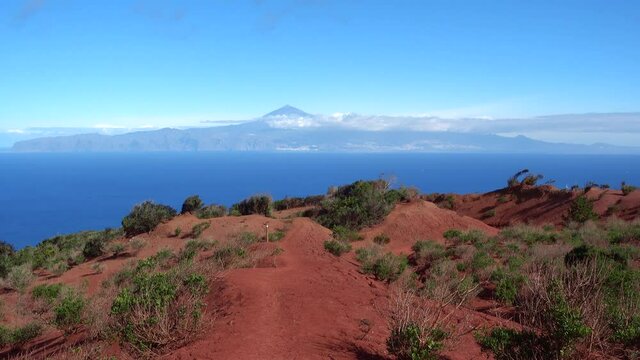 La Gomera - Schwenk &uuml;ber die rote Erosionslandschaft im Norden mit Blick nach Teneriffa, markierter Wanderweg kurz vor dem Mirador de Abrante