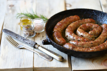 Selective focus. Fried homemade sausages in a frying pan on a wooden surface. Delicious Bavarian sausages.