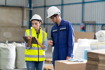 Female Inventory Manager checking stock on Digital Tablet. Man warehouse worker with hard hat safety helmet at storage buildings