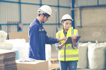 Female Inventory Manager checking stock on Digital Tablet. Man warehouse worker with hard hat safety helmet at storage buildings