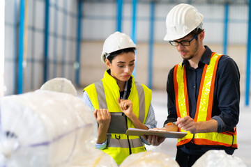 Female Inventory Manager checking stock on Digital Tablet. Man warehouse worker with hard hat safety helmet at storage buildings