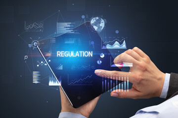 Businessman holding a foldable smartphone with REGULATION inscription, successful business concept