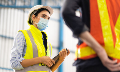 Female Inventory Manager working on digital tablet and checking quality of product at mask factory. Warehouse worker working at storage building.