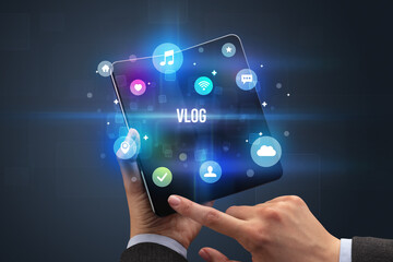 Businessman holding a foldable smartphone with VLOG inscription, social media concept