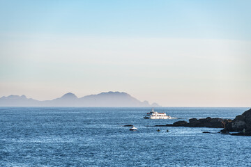 Fototapeta na wymiar A lonely ferry cruises inside the Ria de Pontevedra in Galicia at dusk, with the Cies Islands in the background.