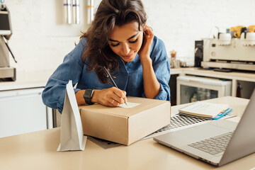 Female business owner working in a coffee shop, makes notes on a cardboard box for delivery