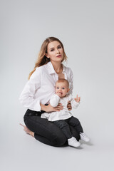 Woman in light clothes have fun with cute child baby girl. Mother, little kid daughter isolated on light wall background, studio portrait. Mother's Day love family, parenthood childhood concept