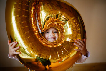 Funny emotional child girl with golden balloon. Children's birthday. Lifestyle and minimalism.