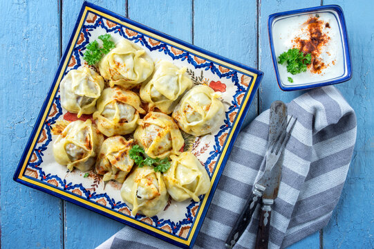 Traditional steamed Russian pelmeni with yoghurt cayenne pepper offered as top view on a rustic design plate