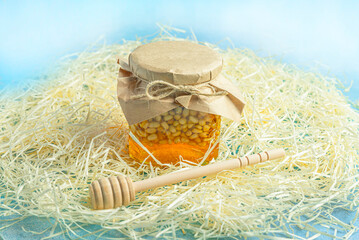 Jar of honey with nuts and honey spoon in a wooden box with sawdust, top view