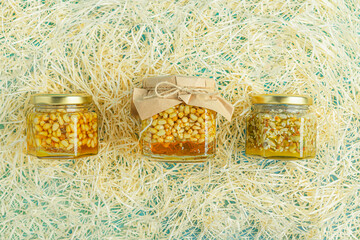 Jar of honey with nuts and honey spoon in a wooden box with sawdust, top view