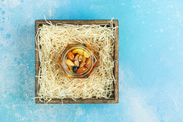 Jar of honey with nuts and honey spoon in a wooden box with sawdust, top view