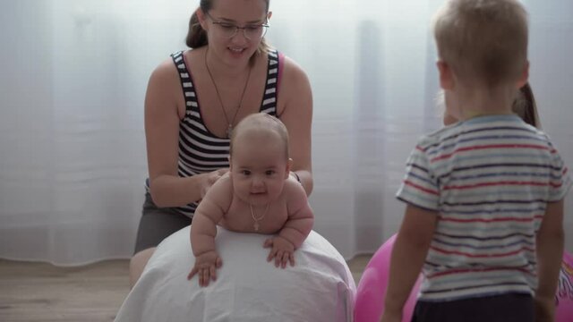 Childhood, Motherhood, games, upbringing, development concept - young mom do exercise, masah with newborn baby on fitball. little daughter girl and boy son play, smile in kid playroom. kids in nursery