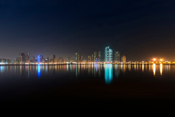 Obraz na płótnie Canvas Beautiful urban city by the sea at night. A panoramic view of Sharjah skyline at night.