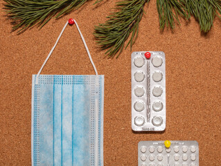 Medical mask and white pills pinned on a corkwood notice board which is decorated with pine twigs...