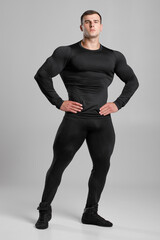 Muscular man in black compression sportswear on gray background