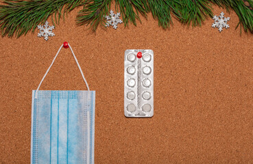 Medical mask and white pills pinned on a corkwood notice board which is decorated with pine twigs...
