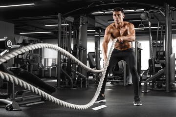 Muscular man working out with heavy ropes in gym. Strong male naked torso abs