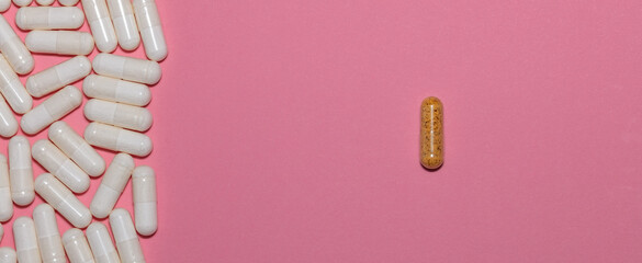 Top view of white pills on one side and a single brown pill on the other side on pink background with copy space. Healthcare, medical and pharmaceutical concept. Banner size.