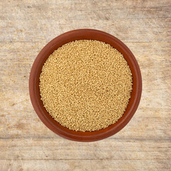 Top view of amaranth seeds in a small bowl on a wood cutting board.