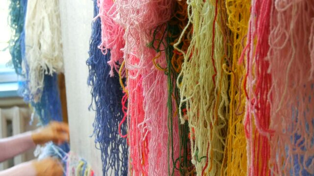 A large number of different woolen threads. Handmade carpet embroidery. Women's hands create a pattern using multi-colored threads. Hammer for embroidery quors, stuffing threads.