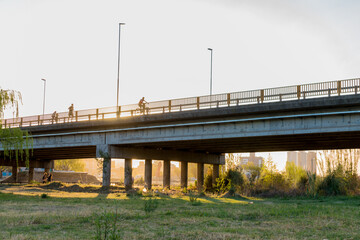 photography of people running and cycling over a bridge at sunset