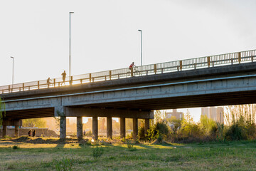 photography of people running and cycling over a bridge at sunset