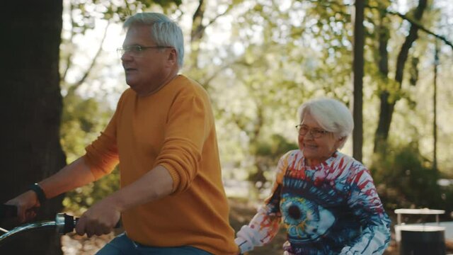 Senior couple riding double bicycle in autumn. Grandmother and grandfather cycling together . Elderly people healthy and active lifestyle. High quality 4k footage