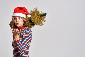 woman with a Christmas tree in her hand yellow tinsel holidays cap gifts New year light background cropped view