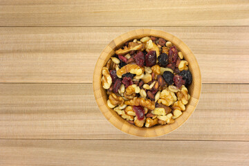 Top view of a bowl of healthy trail mix on a wood background.