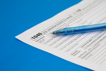 Obraz premium Tax return close-up on a blue background. Blue pen on tax form 1040. Selective focus