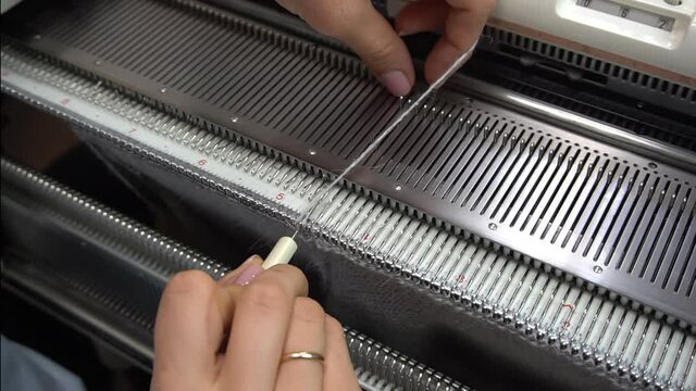 Female hands making textile on weaving machine at factory. Knitting machine Close up of weaving fabric on loom machine. Manufacturing knitted fabric on manual knitting equipment. Textile industry