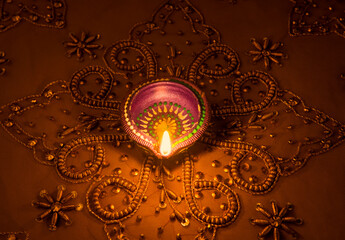 A traditional indian earthen lamp glowing on a golden luxurious embroidered background
