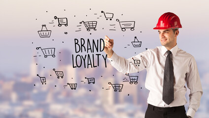 Handsome businessman with helmet drawing BRAND LOYALTY inscription, contruction sale concept