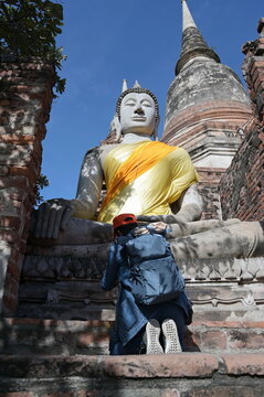 Asian tourists wearing jeans, gray backpack and orange hats pay homage to Buddha statues. Which is a sacred Buddha image in Wat yai chai mongkhon in the city of Ayutthaya north of bangkok in Thailand.