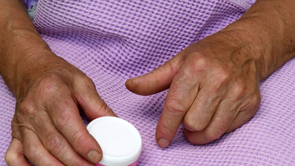 Fototapeta na wymiar Person holding pills in box. Old lady arthritis hands hold cream jar