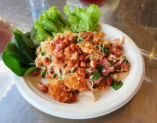Yam Naem Khao Tod: Spicy Pork Salad with Crispy Rice, served with vegetables in recycled paper plates, Thai food spicy popular appetizer made from fried rice and chili paste mixed with marinated pork.