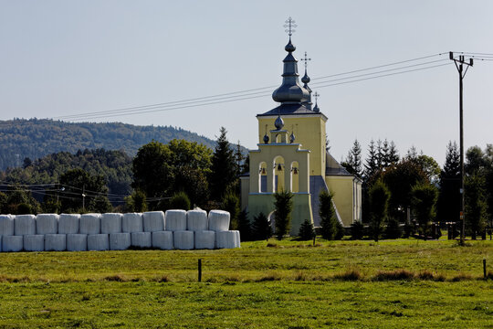 Former Greek-Catholic Lemko church building built in Smerekowiec village in 1818 year. Nowadays Catholic church. Hay rolls covered with plastic in front.