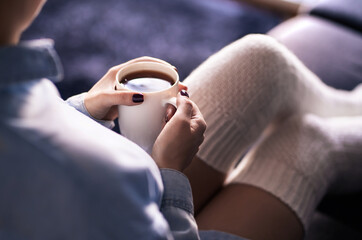 Cup of morning tea in winter. Woman with hot drink and warm cozy long socks on comfy home couch....