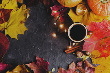 Cozy autumn seasonal composition. Mug of black coffee and autumn maple leaves on dark background.