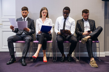 various job candidates sit in line, waiting for an interview, looking through gadgets. Hiring,...