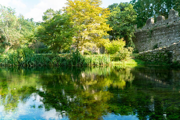 The river of the Garden of Ninfa, medieval stone bridge over the lake, relaxing view, Italy