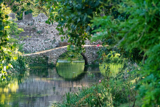 The river of the Garden of Ninfa, medieval stone bridge over the lake, relaxing view, Italy