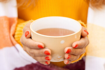 Hands of a young girl holding cup with hot tea. Concept of fall