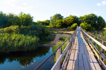 Suspension bridge on the river. Landscape, forest, sunlight, rays, glare, reflection in the water. Template for banner, poster, Wallpaper, puzzles.