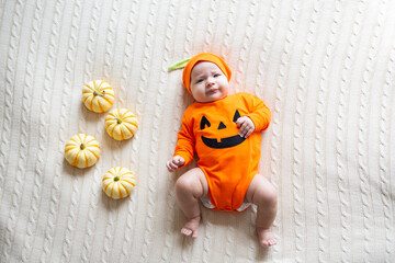 Fototapeta premium High Angle View Of Baby In Pumpkin Costume. Happy Kid two months old in orange Halloween costume on bed